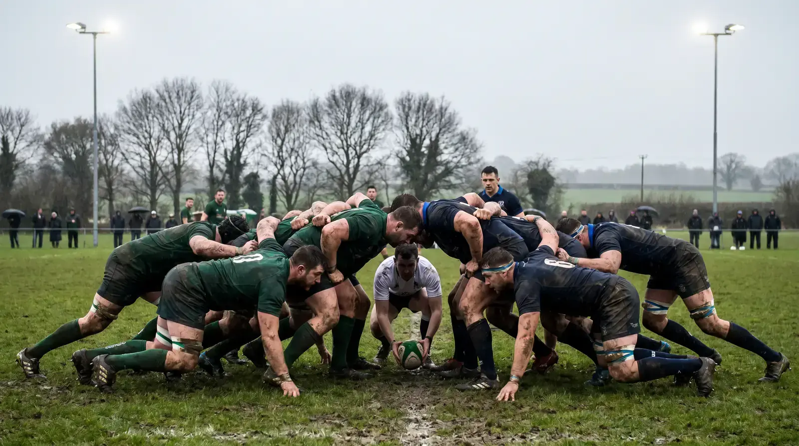 Premiership rugby scrum locked under floodlights on a muddy winter pitch in England