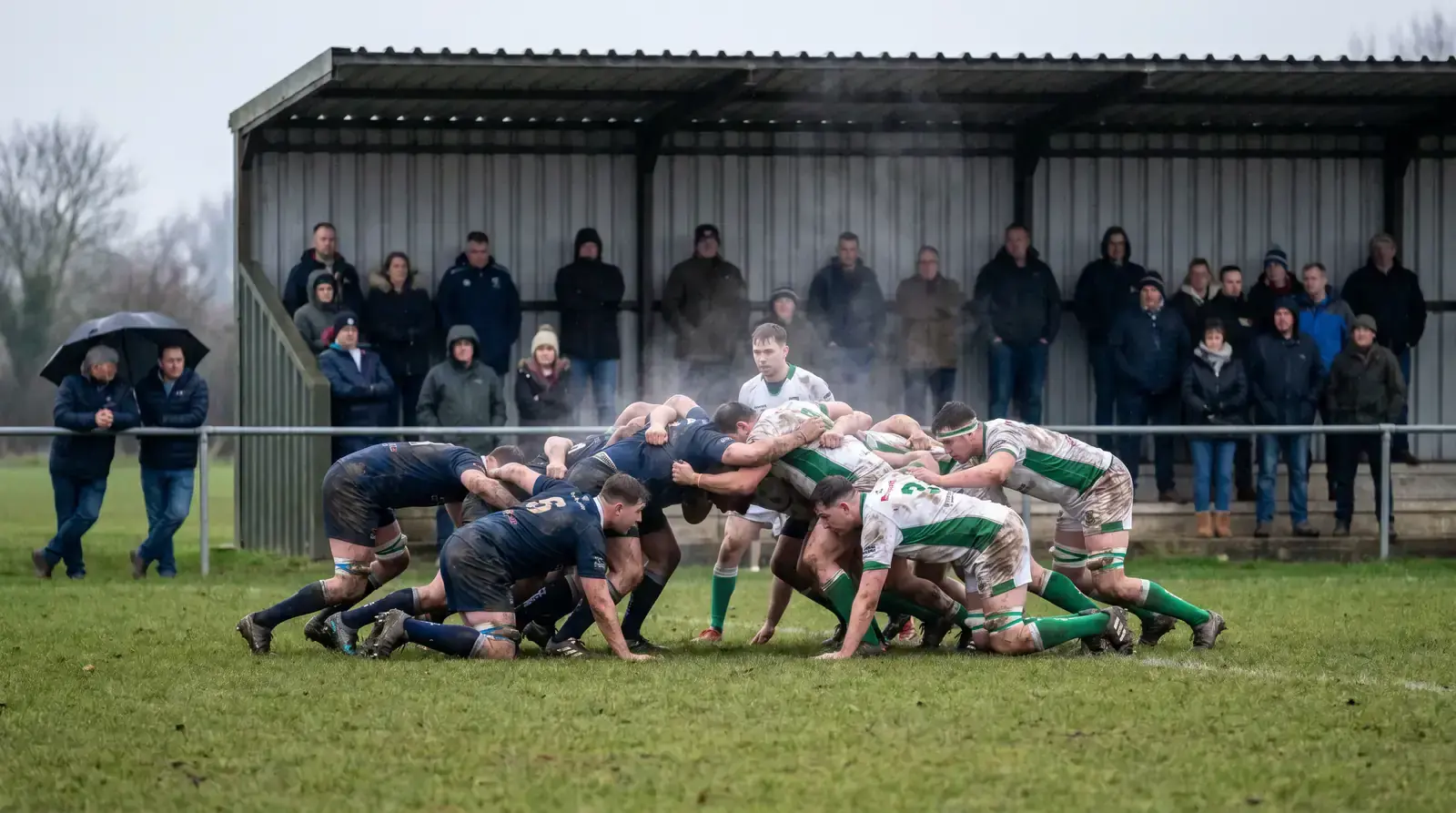 Second-tier rugby match in progress with sparse but engaged crowd