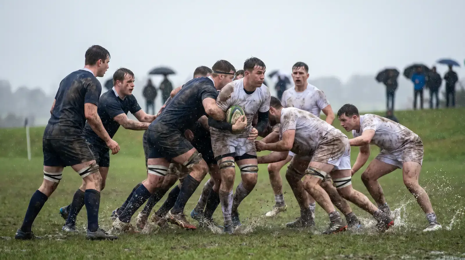 Rugby players in heavy rain contesting a slippery ball on a wet pitch